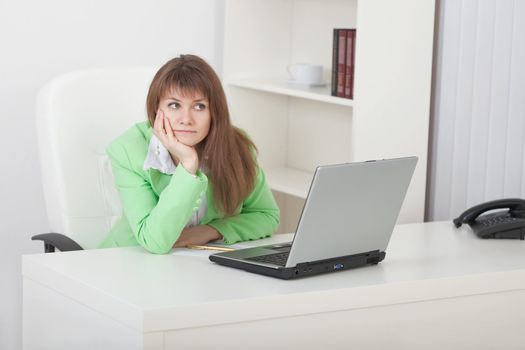 The young woman thoughtfully sits on a workplace at office