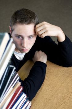 A frustrated and stressed out college student looks up at the high pile of textbooks he has to go through to do his homework assignment.