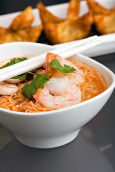 Shrimp and Thai noodle soup bowl with chopsticks along with fried wonton or rangoon type appetizers.