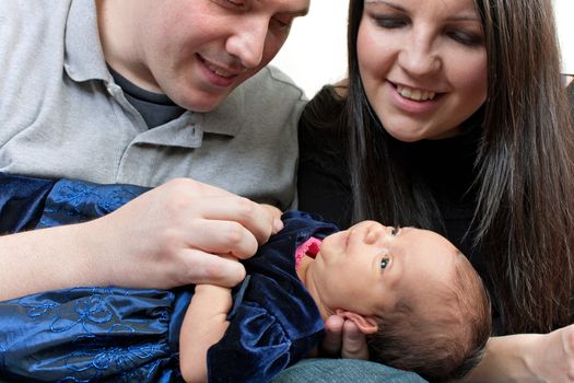 A young happy and healthy family  holding their newborn daughter on their laps.