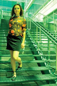 twenty something fashion model coming down outdoor stair made of steel near a glass covered building