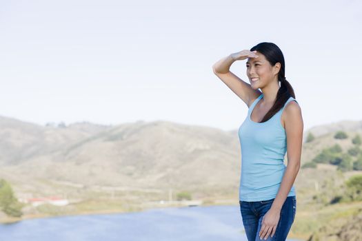 Smiling Young Asian Woman Shielding Eyes Standing in Landscape