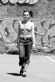 Twenty something urban fashion walking in front of a graffitti wall at high noon