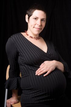 Sitting portrait of a late twenty pregnant women looking at the camera with a shy smile