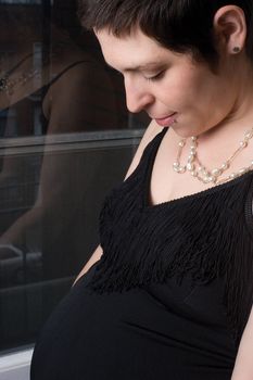 Portrait of a late twenty pregnant women standing in front of a window with urban decor, looking at her belly