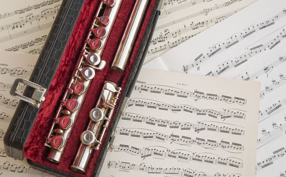 A western concert flute inside its leather and velvet case leant against old music sheets.