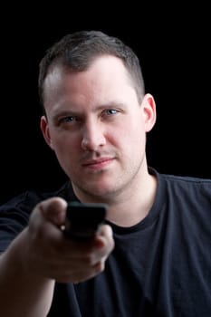 A man in his late 20s changes the television channels with the remote control isolated over a black background. Shallow depth of field.