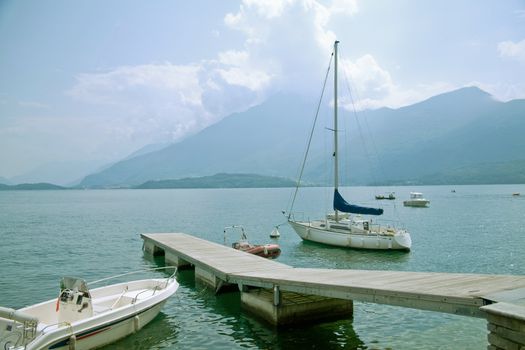 Panoramic view of Lake Como in summer with boats and a wooden jetty on the front.