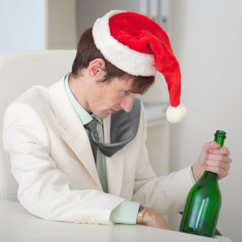 The drunk man in a Christmas cap with a bottle sits at a table