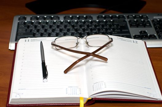 Open weekly journal, glasses and the handle behind a desktop.