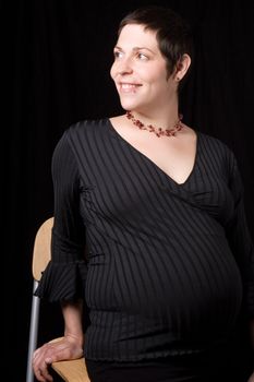 Sitting portrait of a late twenty pregnant women with a great big smile looking to the far right, hand place on seat of the chair