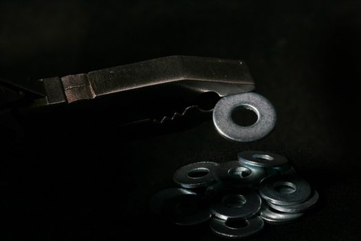 Fixing plain washer in flat-nose pliers and washers on a background.