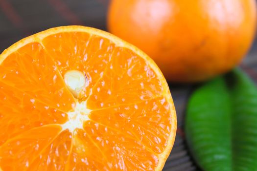 The cut tangerine against a bamboo napkin and the whole tangerine with green sheet removed close up