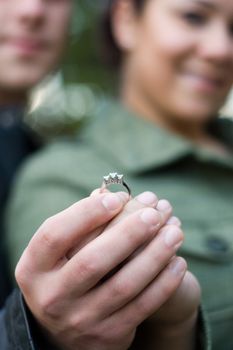 A young happy couple holding a diamond engagement ring.  Shallow depth of field with focus on the ring.