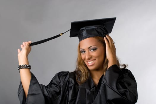 A recent graduate posing in her cap and gown isolated over a silver background.