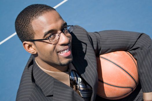African American man in a business suit posing with a basketball.  He could be a coach player recruiter scout or trainer.