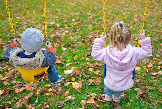 Youthful image of two young children sitting in swings at a playground.