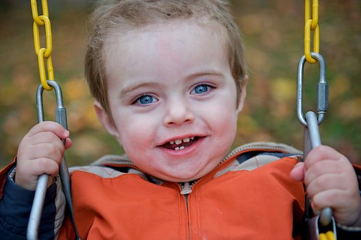 Cute toddler laughing while grasping onto the chains of a swing.