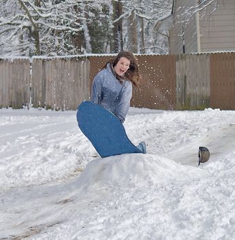 Teen girl jumping a snow mound on a sled after a winter storm.  