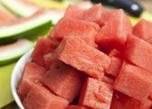 Diced watermelon in a white bowl with green rind and large knife in the background.