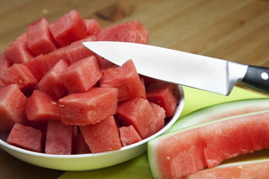 Freshly cut watermelon in a bowl on a kitchen bench, with knife and rind.