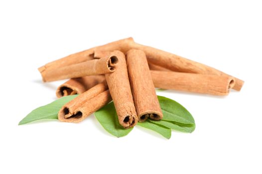 Cinnamon and green leaves. A heap of sticks of cinnamon on a white background