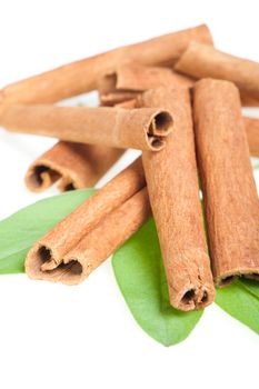 Cinnamon and green leaves. A heap of sticks of cinnamon on a white background