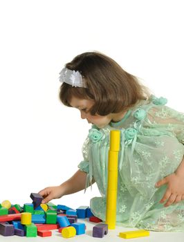 The lovely little girl plays colour wooden cubes. It is isolated on a white background