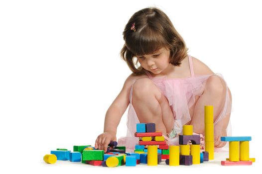 The lovely little girl plays colour wooden cubes. It is isolated on a white background