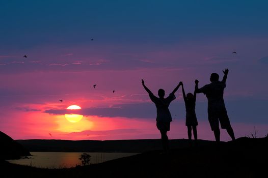 The family from three persons welcomes the sunset sun.