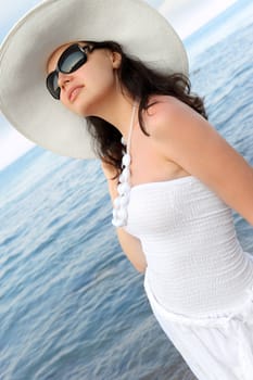 The woman on seacoast. In sun glasses, a sundress, a hat.