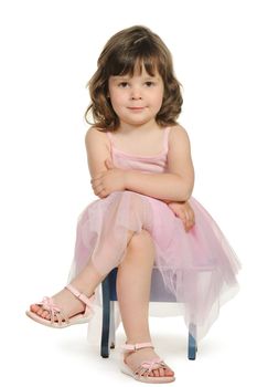 Pretty the little girl sits on a stool. It is isolated on a white background