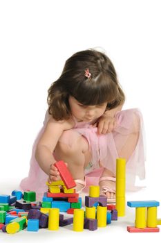 The lovely little girl plays colour wooden cubes. It is isolated on a white background