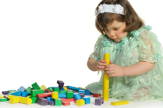 The lovely little girl plays colour wooden cubes. It is isolated on a white background