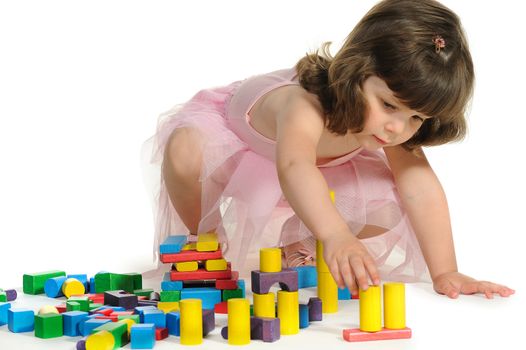 The lovely little girl plays colour wooden cubes. It is isolated on a white background