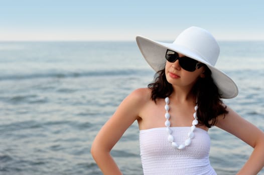 The woman on seacoast. In sun glasses, a sundress, a hat.