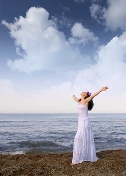 The woman in a white sundress on seacoast with open hands. Cloud sky