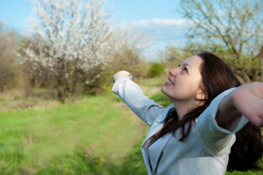 The happy attractive woman with the lifted hands. Against the spring nature