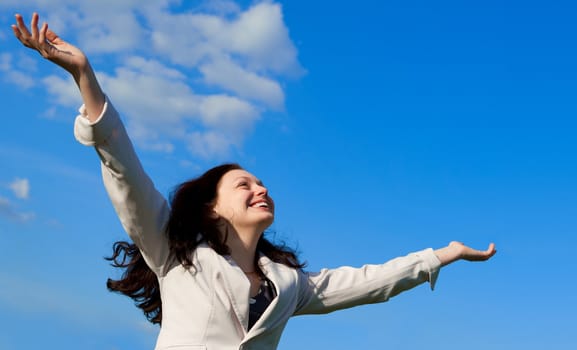 The happy attractive woman with the lifted hands. Against the blue sky