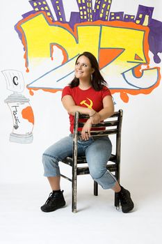 Young women with great big smile sitting on a ruff up chair in front of a graffiti background