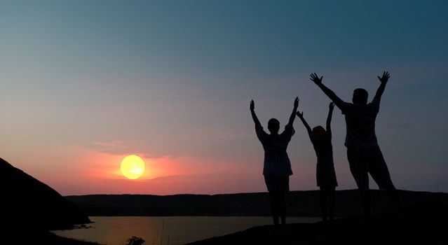 The family from three persons welcomes the sunset sun.