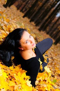 The attractive woman in autumn forest. Lies on yellow leaf