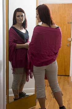 Young woman standing in front of mirror adjusting shawl