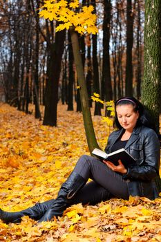 The attractive woman reads the book in autumn forest.