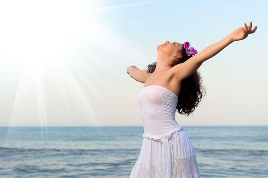 The woman in a white sundress on seacoast with open hands. Sun light