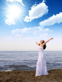 The woman in a white sundress on seacoast with open hands. Cloud sky