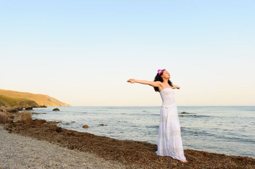 The woman in a white sundress on seacoast with open hands. A picturesque landscape