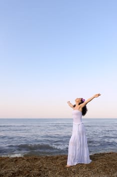The woman in a white sundress on seacoast with open hands. A picturesque landscape