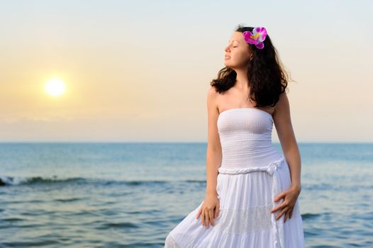 The woman in a white sundress on seacoast. Sunset illumination