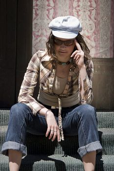 Teen girl sitting on stair of a front porch, adjusting her sunglasses